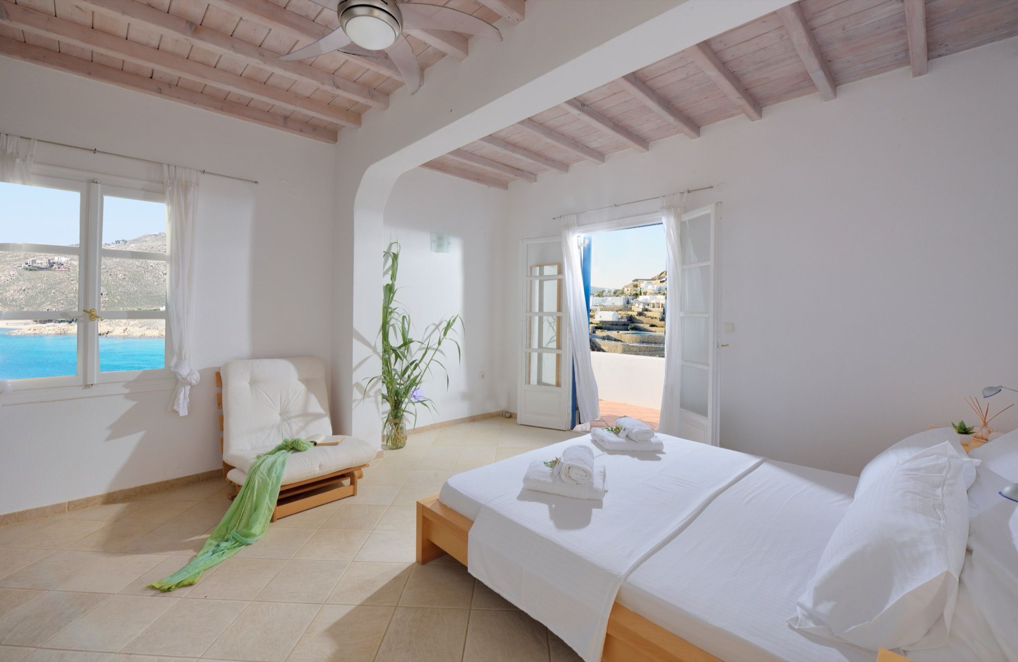 Bright bedroom under a beamed ceiling, with a double bed, an armchair and a window to the sea