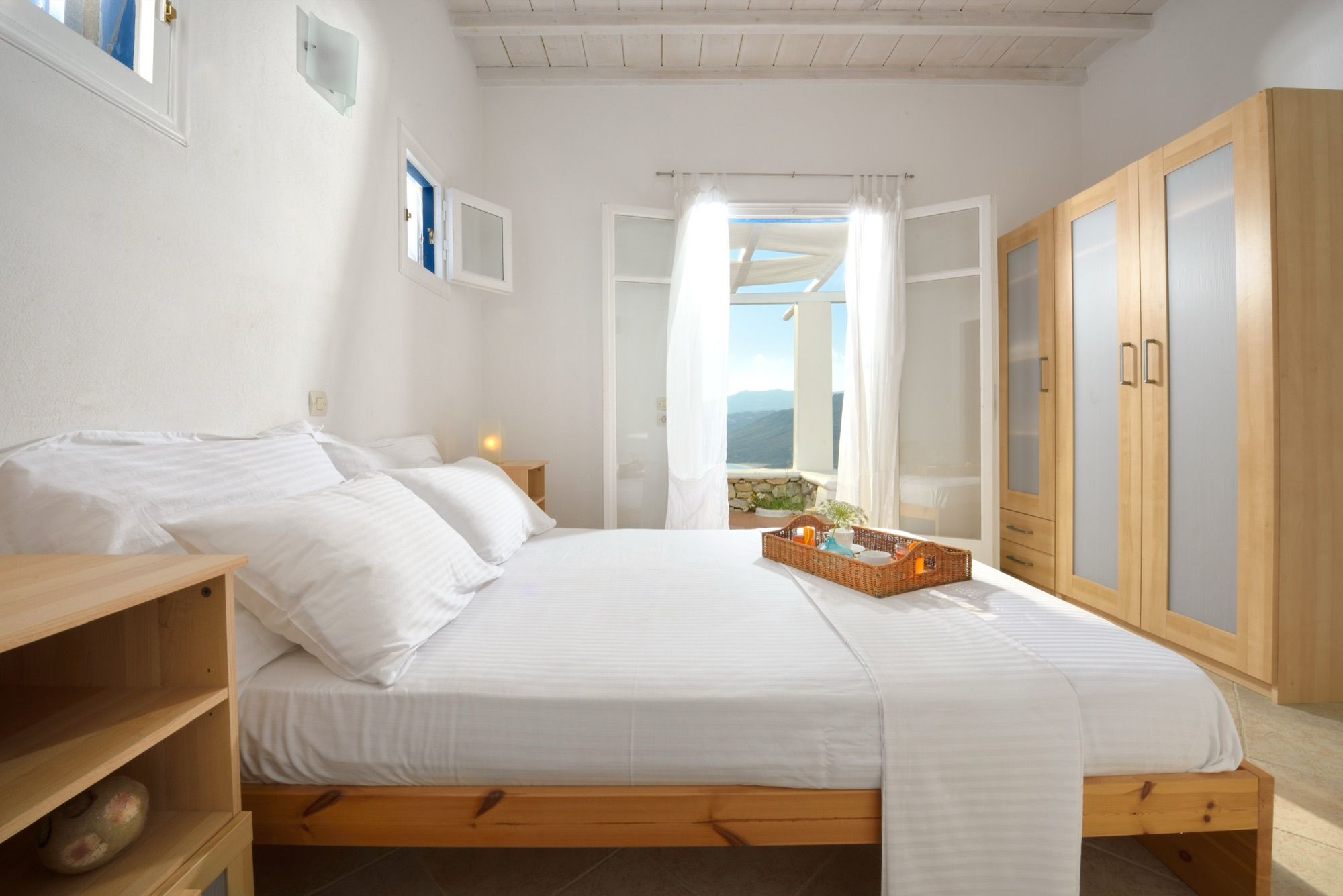 White bedroom with a king-size bed, wardrobe and doors to a terrace with a sea view