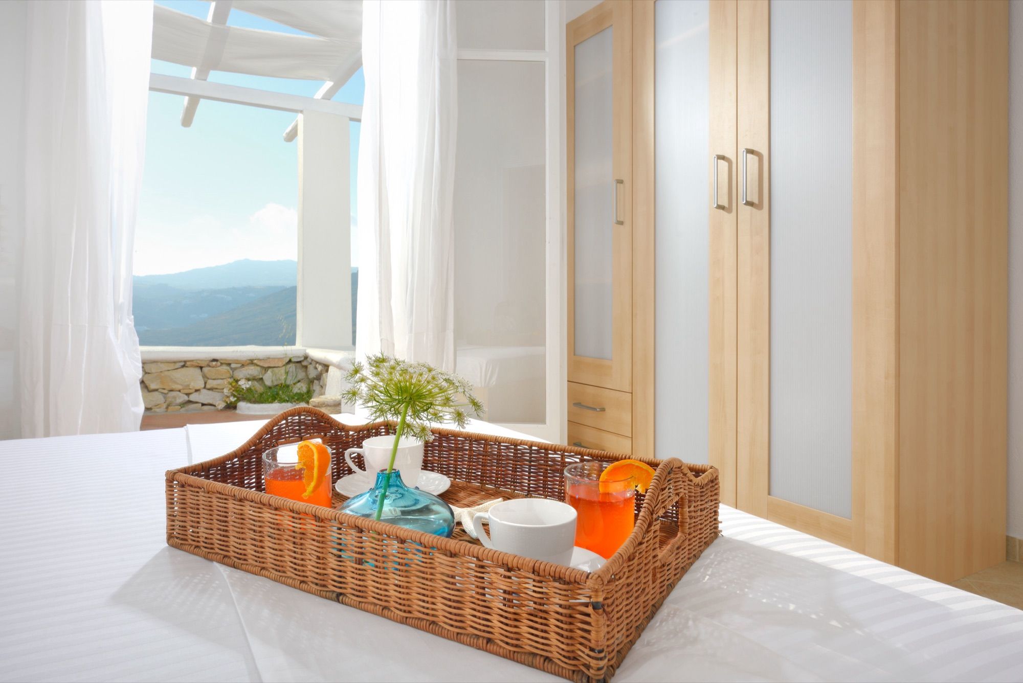 Breakfast tray with juice and coffee on a made bed, the sea visible through the window