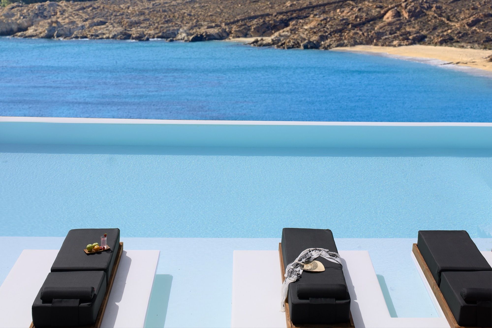 Sunbeds set in the shallow ledge of the infinity pool, with Elia bay beyond