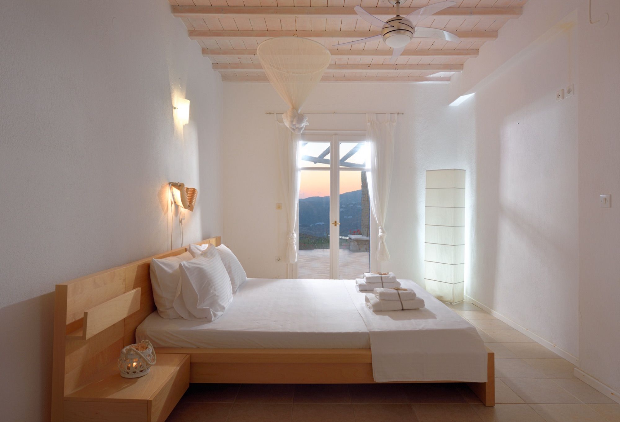 Bedroom with a double bed and glass doors to the terrace at sunset