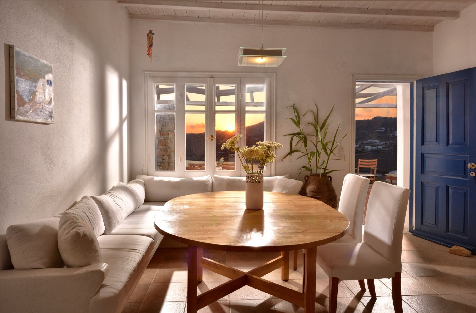 Dining corner with an oval wooden table and built-in sofa, sunset through the windows