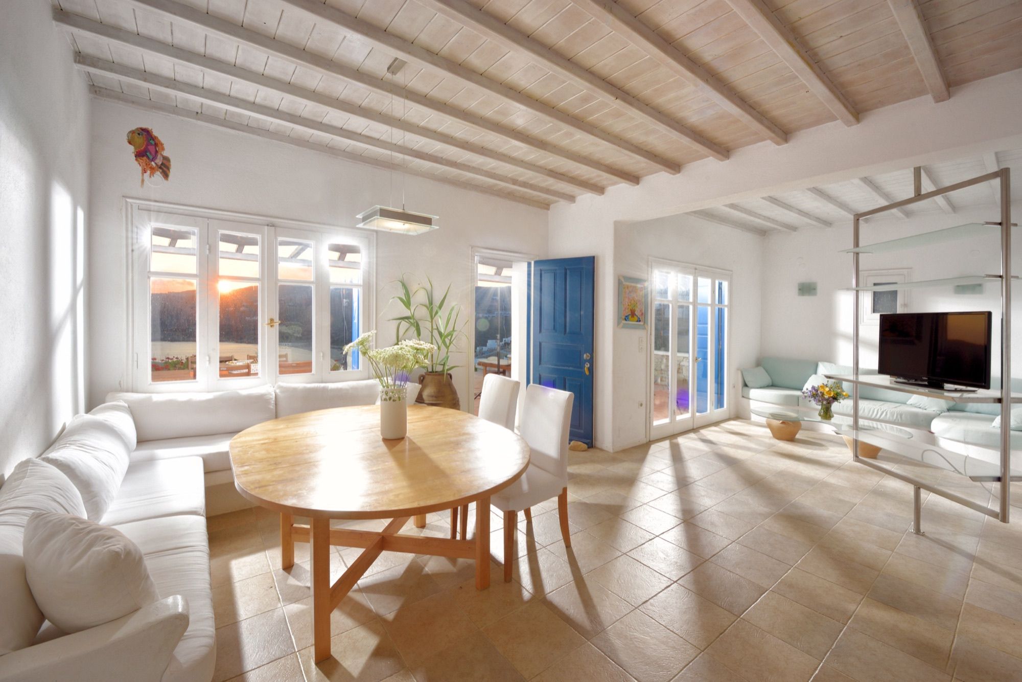 Living and dining room with a round wooden table, built-in sofa and sunset light through the windows