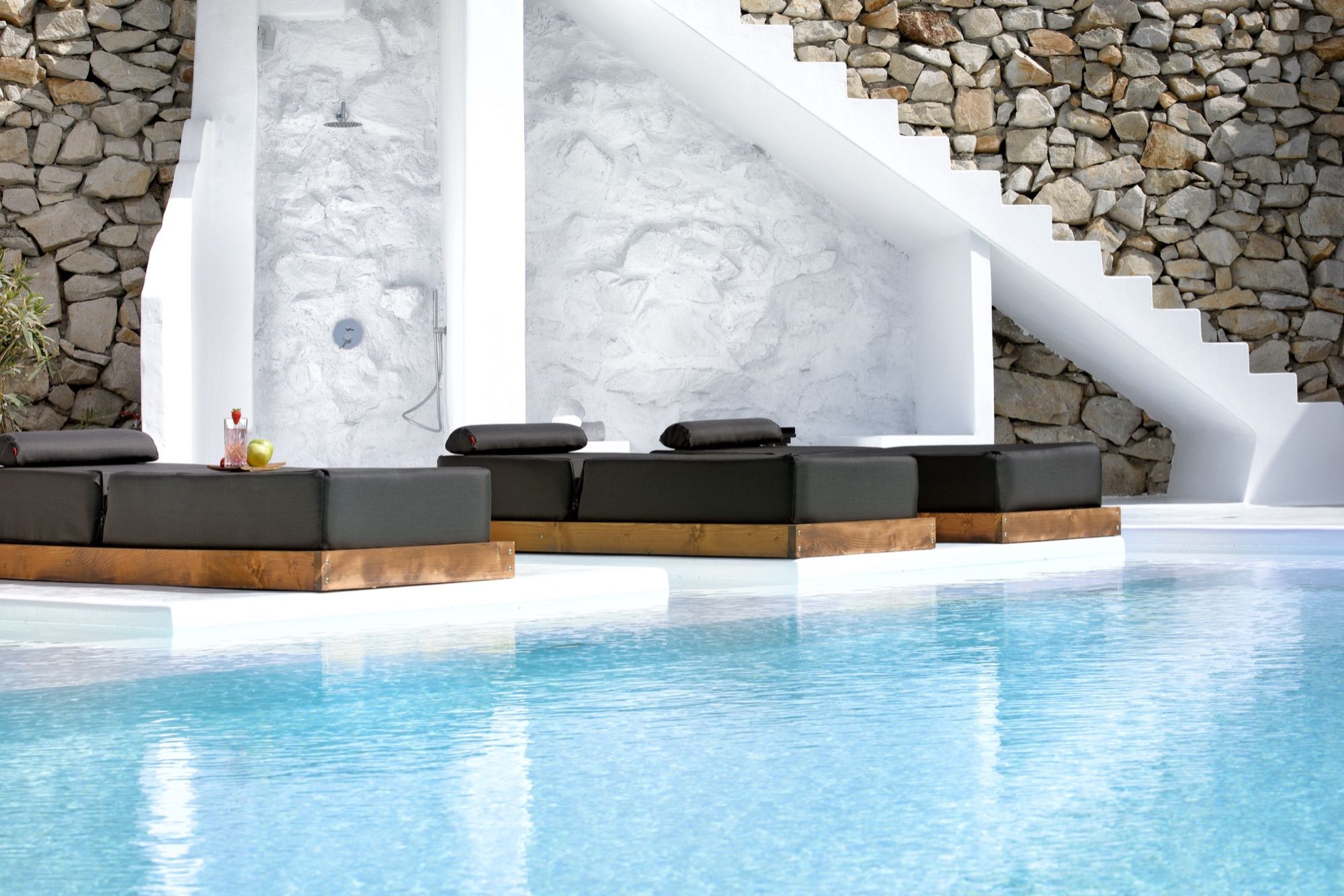 Outdoor shower set in a white sculpted wall under the stone stairs, beside the pool sunbeds