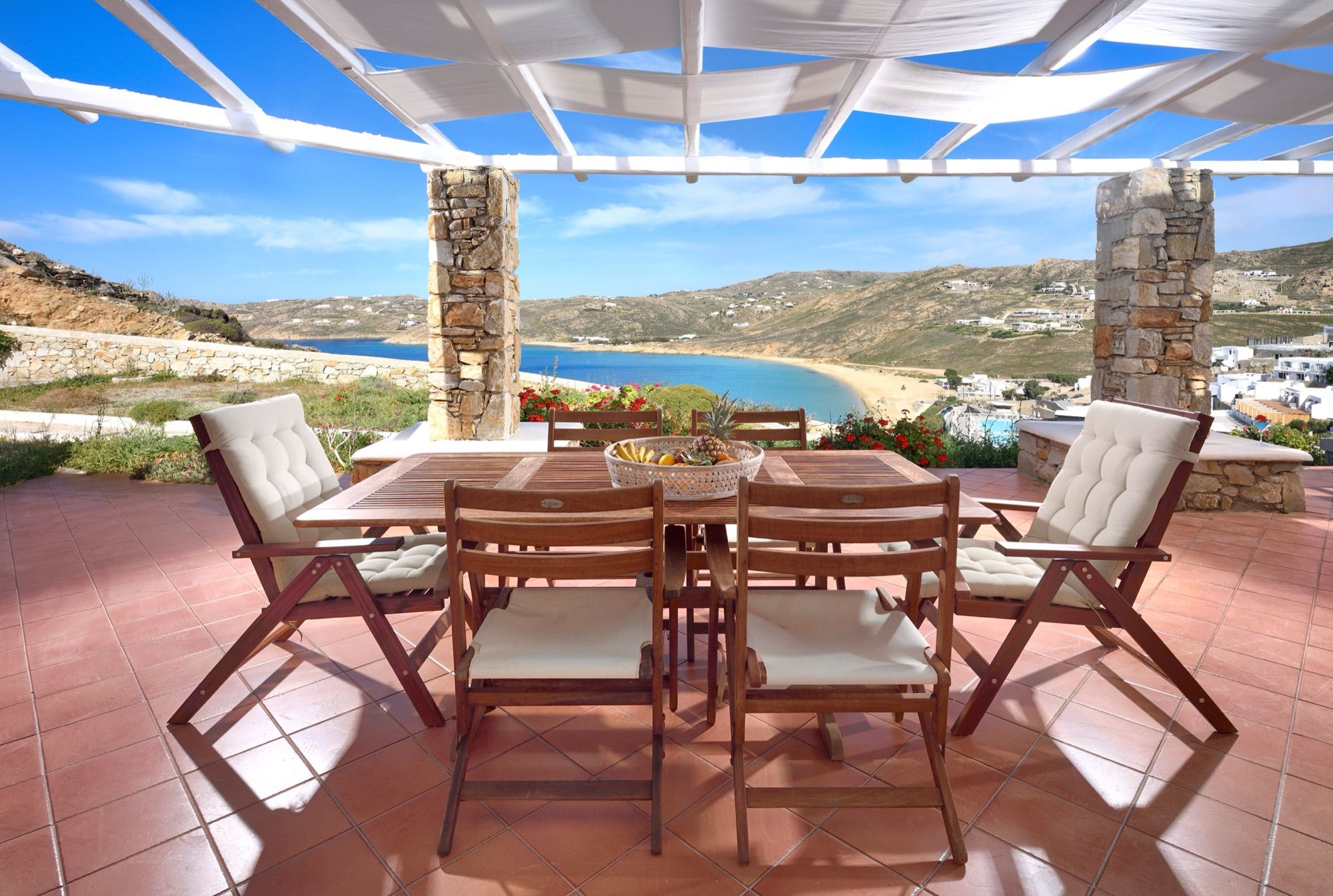 Shaded dining terrace under a pergola with stone pillars and a view of Elia Beach