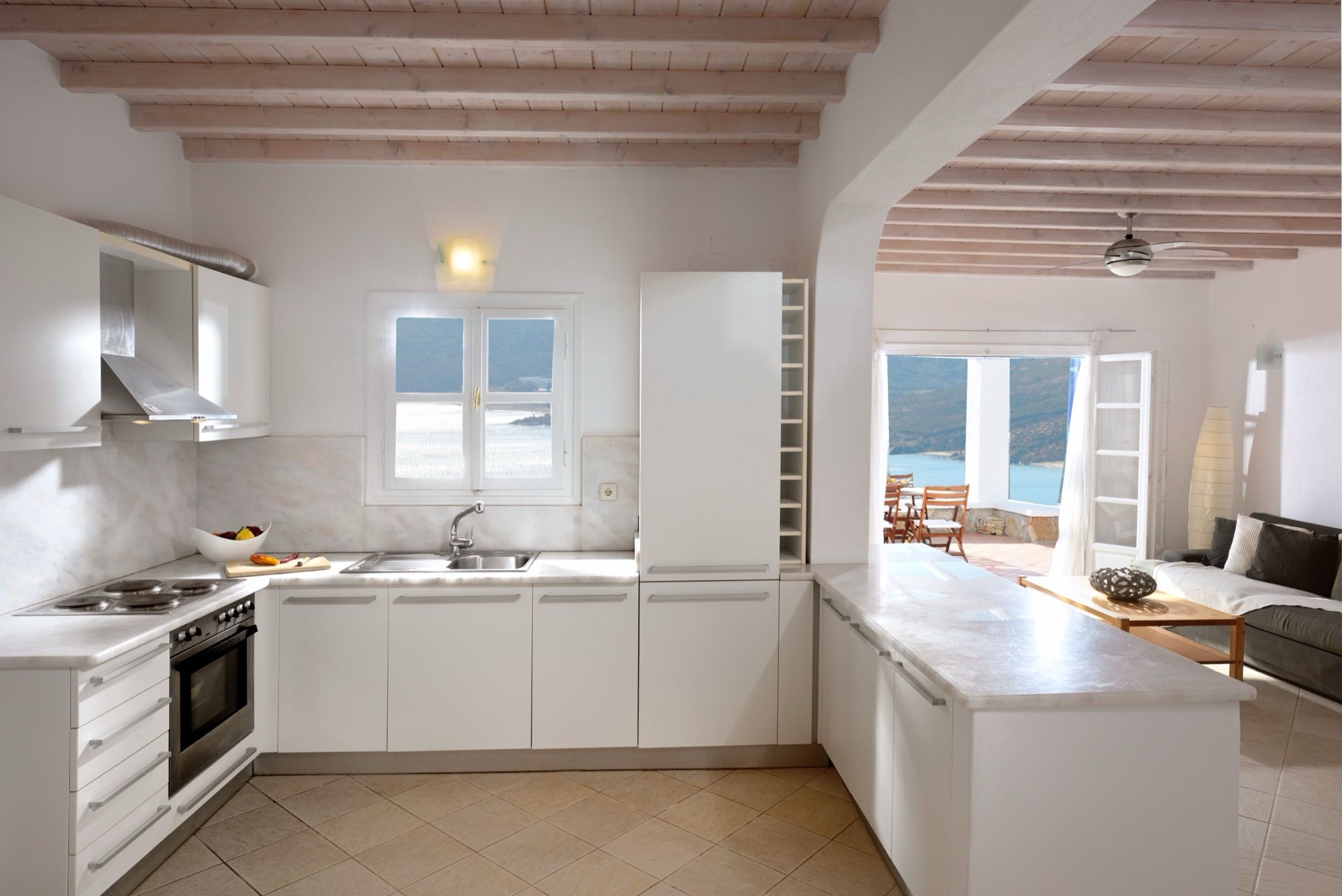 White fitted kitchen with oven and hob, open to the living room and terrace