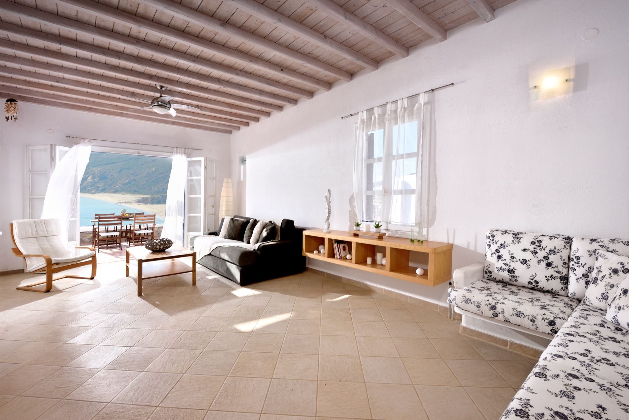 Wide living room with sofas, wooden beams and windows to the sea