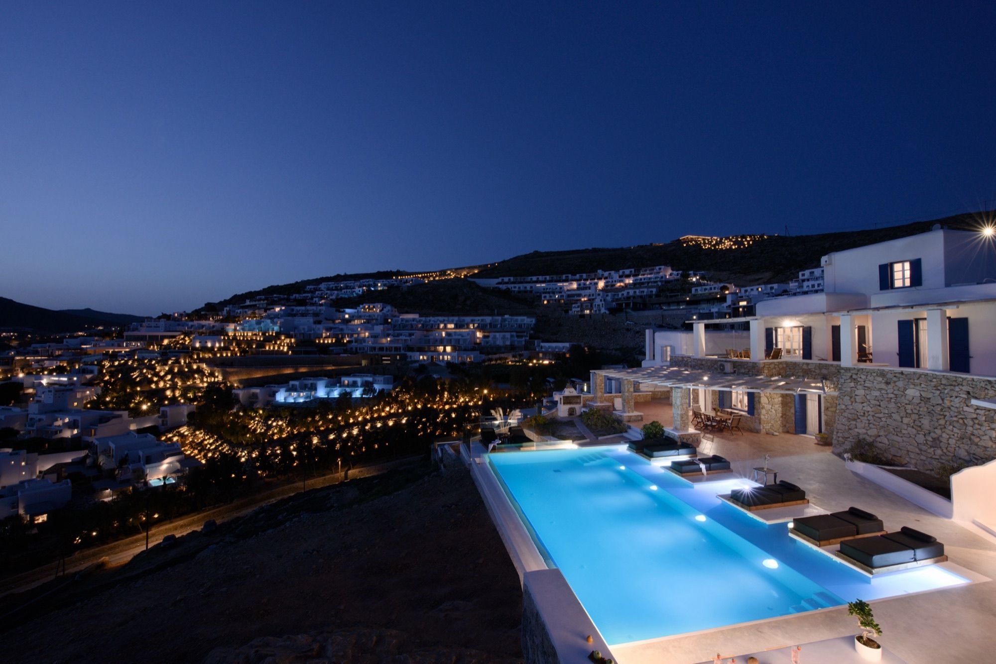 The villa and its long pool at night, with the lights of Elia hillside below