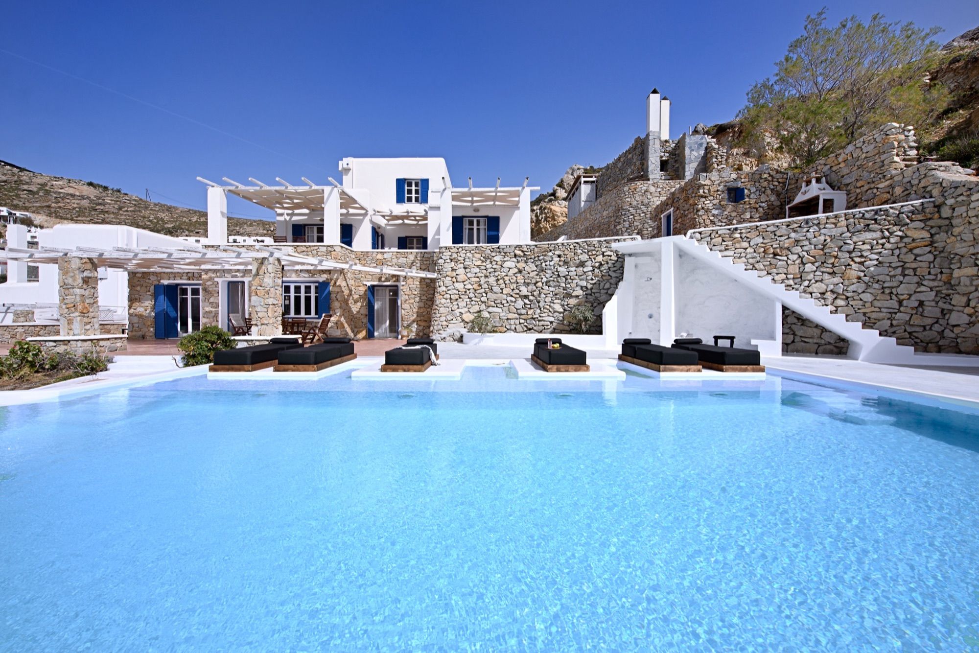 The whitewashed villa with blue shutters and stone walls rising above the pool